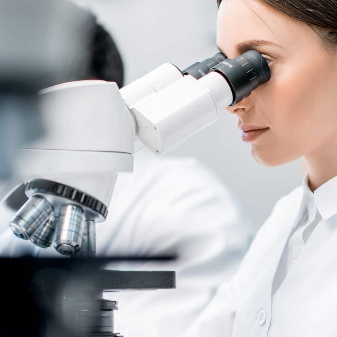 A vet in a lab coat examines a sample through a microscope in a laboratory setting